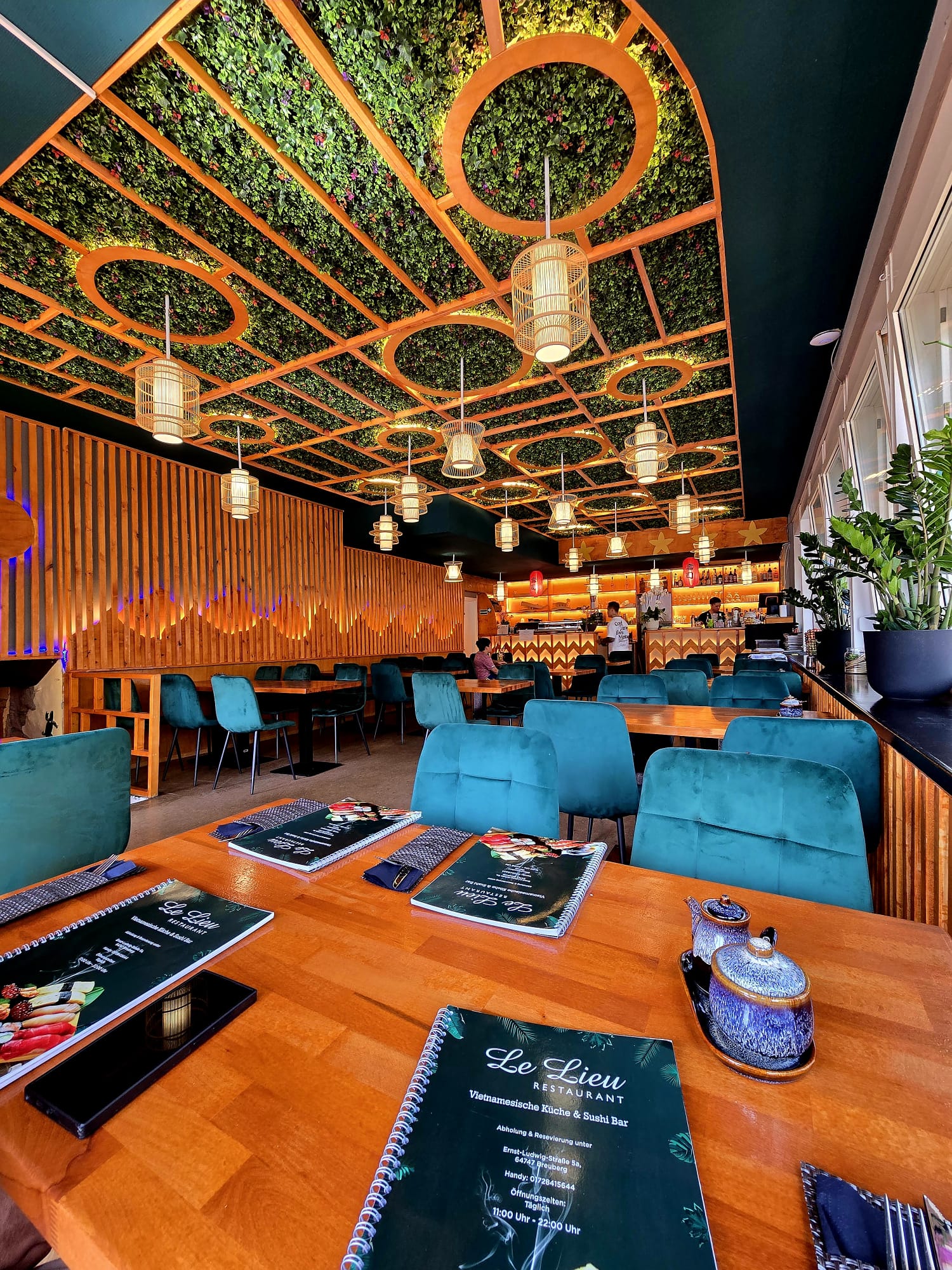 Gastraum des Lê Lieu Restaurant mit begrüntem Deckenelement und Rattan-Lampen